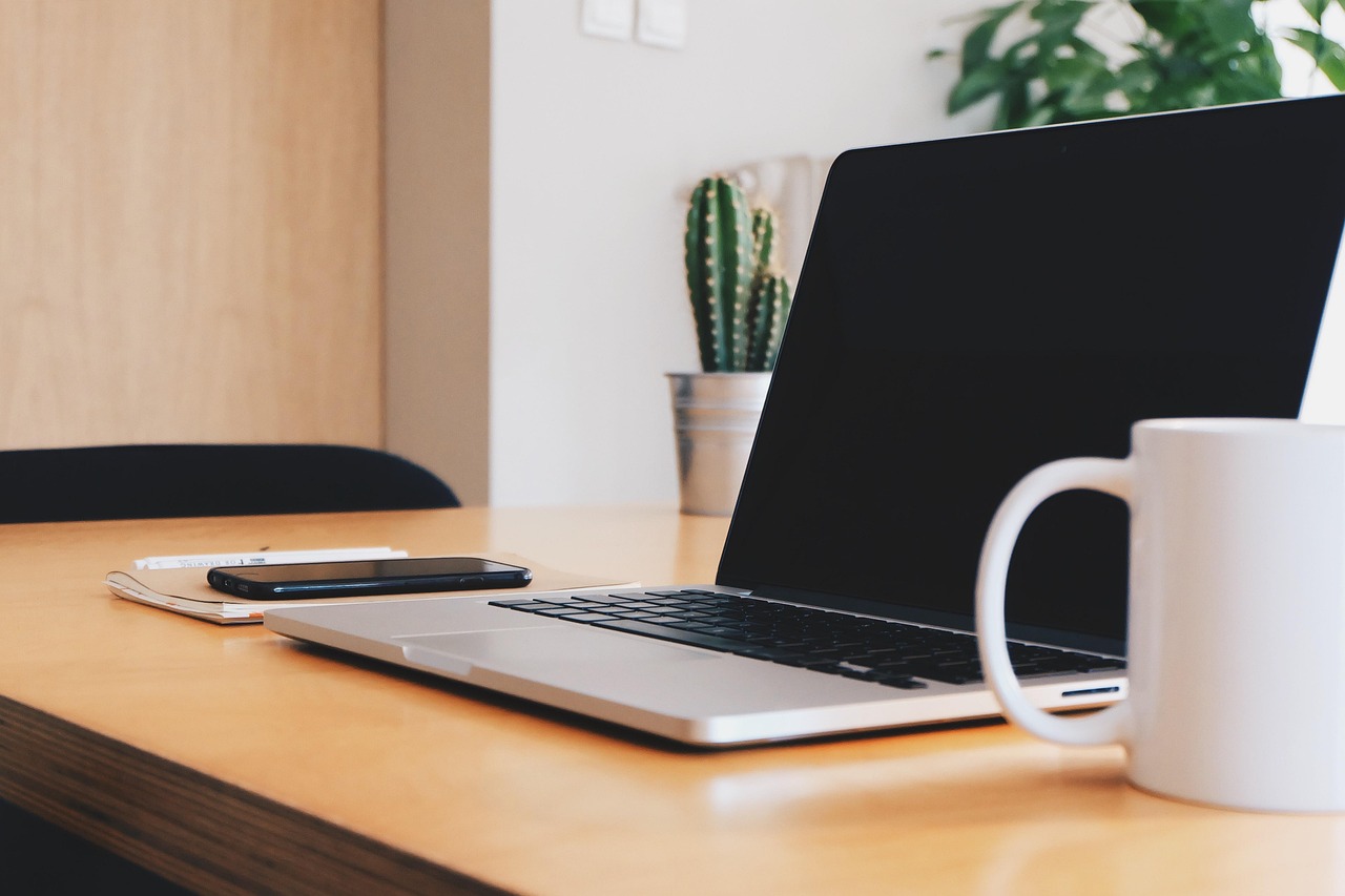 Image of a laptop, phone, mug and notebook on a desk